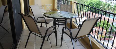 A balcony with a round table and four chairs, a small folding table, and a green doormat.