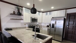 A modern kitchen with a central island, stainless steel appliances, and a dark ceiling light. - Summer in Playa Flamingo Costa Rica. 2bd/2bath Sleeps 6 Ocean View,new upgrade (Playa Flamingo)