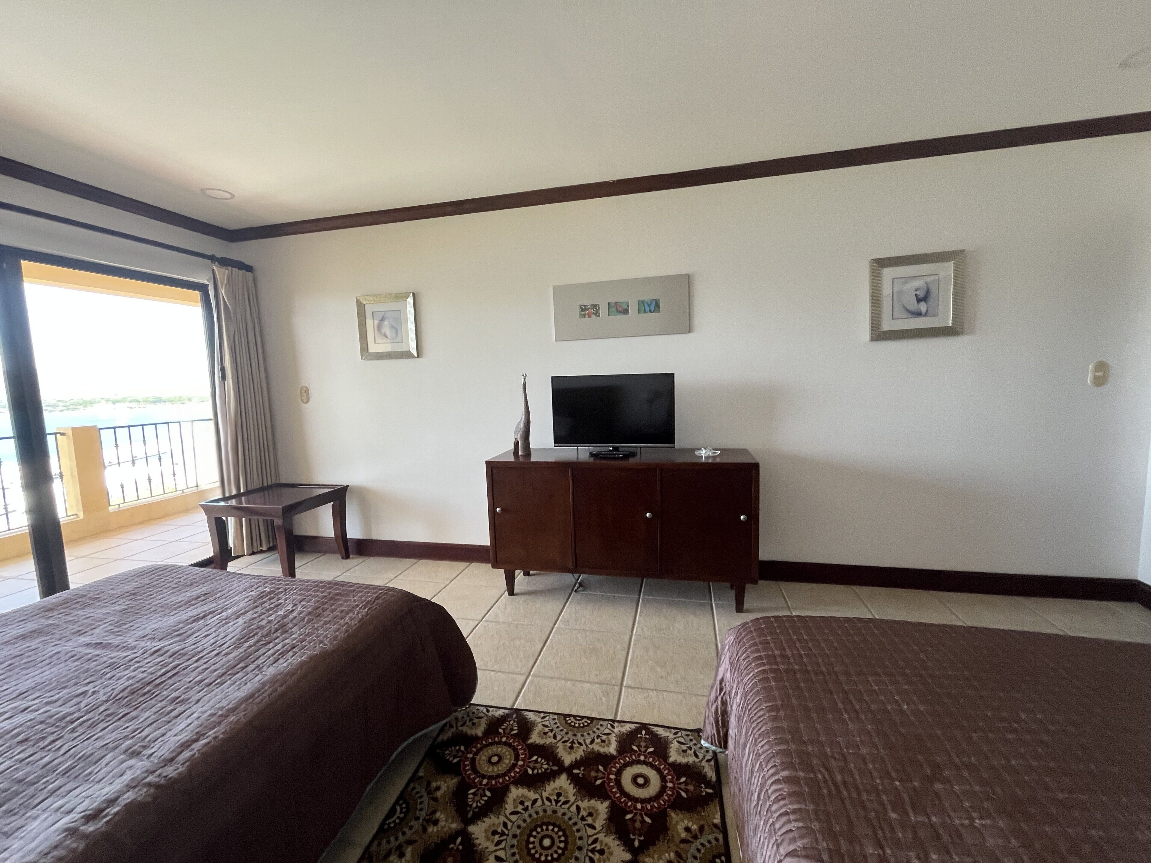 Ein Hotelzimmer mit zwei Betten, einem Fernseher auf einer Holzkommode und einem Balkon mit Blick.