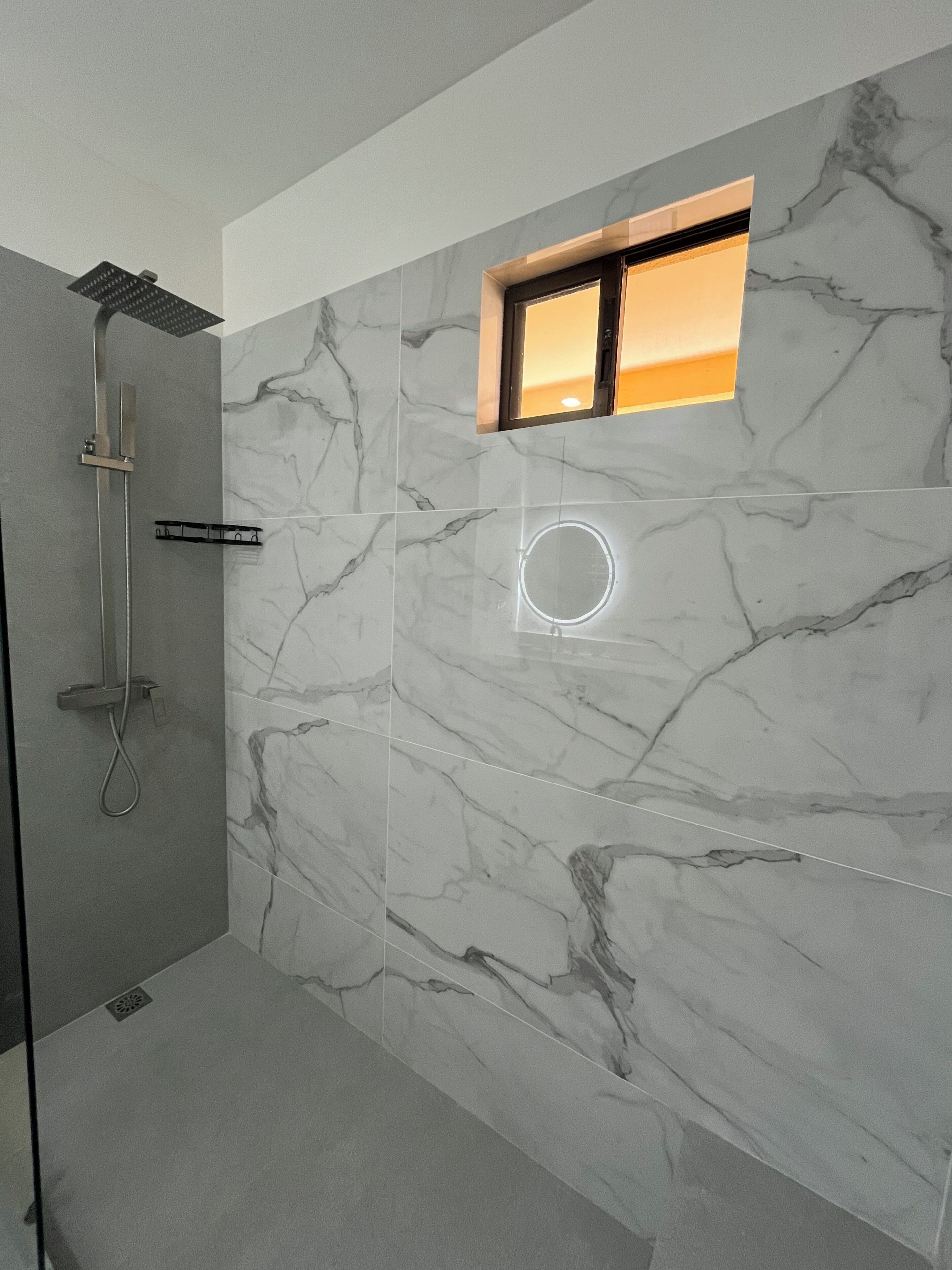 A modern bathroom with a shower, marble walls, and a circular light fixture.