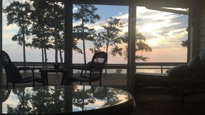 A room with a glass table reflecting trees and sky, two chairs, and a sofa with cushions. - Sunset Lodge on the Bay (Rock Hall)