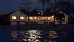 A waterfront house with a stone wall, large windows, and a visible deck area. - Sunset Lodge on the Bay (Rock Hall)
