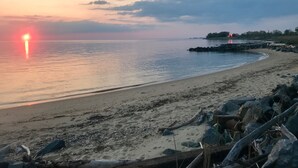 A beach with a calm sea, a sunset, and a rocky shoreline. - Sunset Lodge on the Bay (Rock Hall)