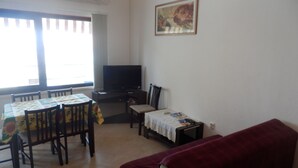 Un salon avec un téléviseur, une table à manger avec des chaises, un canapé et un tableau accroché au mur.