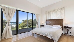 A bedroom with a large bed, two bedside tables, and a view through a sliding glass door to an outdoor area. - IL Mare (expansive ocean views)  (Apollo Bay/ Skenes Creek)