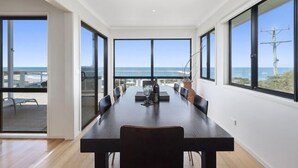 A spacious dining area with a long table and chairs, large windows offering a view of the ocean and beach, and a modern interior design. - IL Mare (expansive ocean views)  (Apollo Bay/ Skenes Creek)