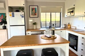 A modern kitchen with wooden countertops, a built-in oven, and a dishwasher. There is a window with a view of greenery outside. - Lake & Reserve Front Bird Haven - 3BR (Encounter Bay)