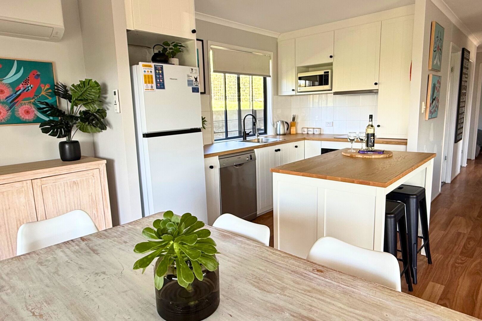 Une cuisine moderne avec des meubles blancs, un îlot central et un coin repas comprenant une table et des chaises.