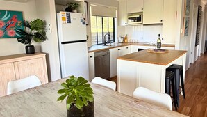 Ett modernt kök med vita skåp, en köksö och en matplats med bord och stolar.