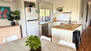 Une cuisine moderne avec des meubles blancs, un îlot central et un coin repas comprenant une table et des chaises.