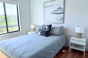 A bedroom with a large bed, two bedside tables, a window with a view, and a framed picture on the wall.