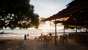 A beachside restaurant with outdoor seating, overlooking the ocean, and a sunset in the background. - Sunset Bliss Andaman Sea View (Klong Muang)