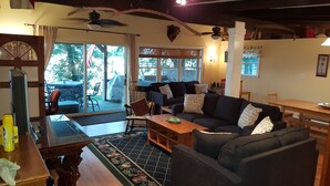 A cozy living room with a dark-colored sofa, a wooden coffee table, and a dining table. There is a large window with a view of the outdoors, and a ceiling fan is visible. - 5-bedroom vacation home 5 minutes from historic Charlestown (Perryville)