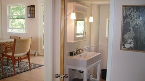 A bathroom with a white sink, mirror, and two wall-mounted lights. There is a wooden door leading to a dining area with a table and chairs. - 5-bedroom vacation home 5 minutes from historic Charlestown (Perryville)