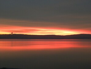 Un lago tranquilo al atardecer con el perfil de una colina a lo lejos.