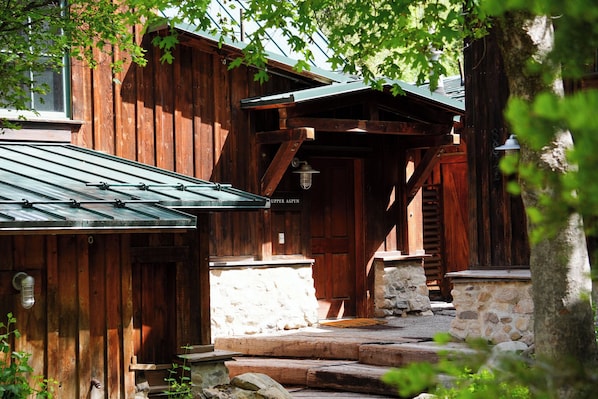 A rustic wooden building with a stone foundation, a metal roof, and a wooden door labeled 'Upper Aspen.'