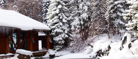 A cabin with a snow-covered roof and a pond in front.