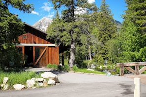 A rustic wooden building with a large entrance, surrounded by lush greenery and a mountain backdrop.