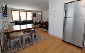 A kitchen with a stainless steel refrigerator, wooden dining table, and a red leather sofa. - Updated Dennis Port Cottage Near Nantucket Sound (2069) (Dennis Port)