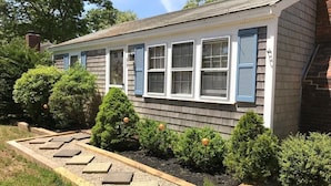 Une maison avec un porche à l’avant, un jardin agrémenté d’un chemin de pierres et des arbustes taillés.