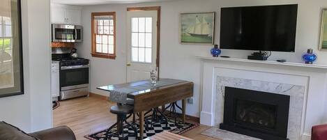 Una sala de estar con chimenea, televisor, mesa de comedor y una zona de cocina con electrodomésticos.