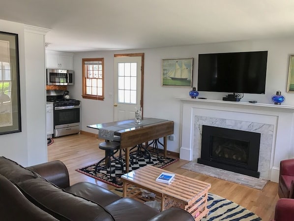 A living room with a fireplace, a television, a dining table, and a kitchen area with appliances.