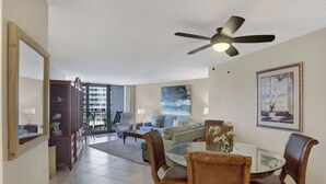 A spacious living room with a ceiling fan, a dining table with chairs, a sofa, a coffee table, and a large window with a view. - Beachfront 2BR in South Seas T3-508 with Updated Kitchen! (Marco Island)