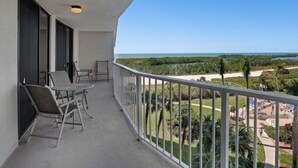 A balcony with a table and chairs, overlooking a beach and greenery. - Beachfront 2BR in South Seas T3-508 with Updated Kitchen! (Marco Island)