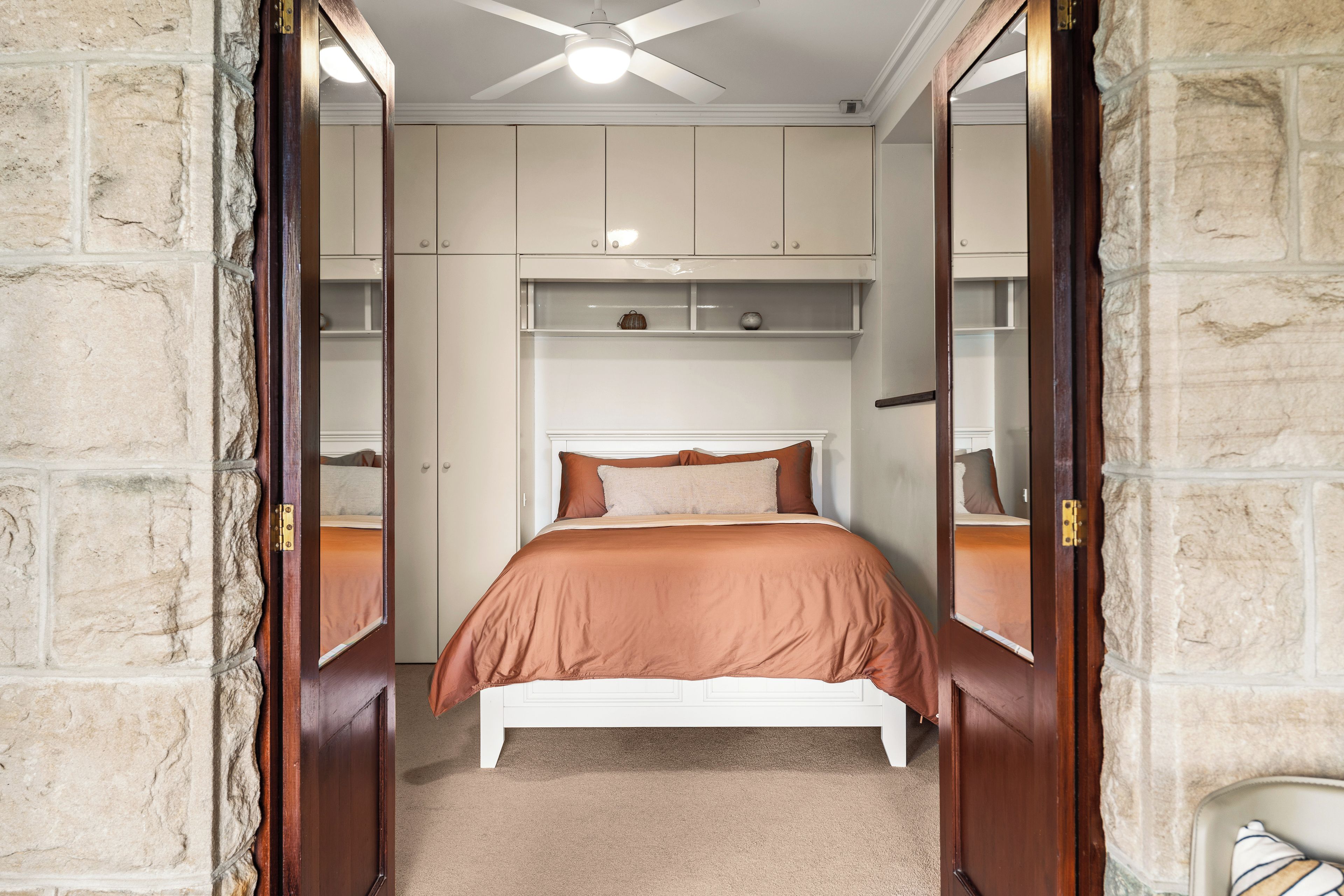 A bedroom with a bed, a ceiling fan, and built-in shelving.
