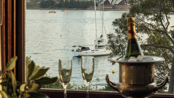 A view of a city skyline with a body of water in the foreground, a bottle of champagne, and two wine glasses on a windowsill.
