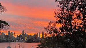 Silhueta urbana ao pôr do sol, com barcos na água.