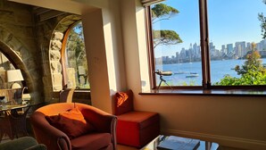Sala de estar moderna com uma janela grande que oferece vista para o horizonte urbano e para a água.