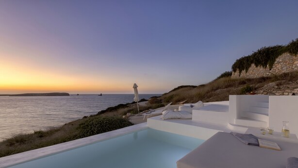 Ein moderner Poolbereich im Freien mit Blick auf das Meer und einen Sonnenuntergang.