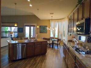 Una cocina con una isla central, armarios de madera, lavavajillas de acero inoxidable y un comedor con sillas y mesa.