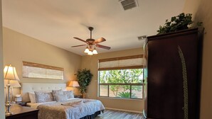 A bedroom with a bed, a ceiling fan, a window with a view of greenery, a wooden floor, and a dark-colored wardrobe. - Casa Bella-Luxury home on corner lot, bring your fur baby. (Oro Valley)