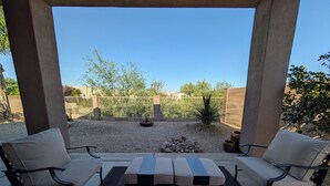 A covered patio with two sofas and a table, a gravel area with plants, and a view of a fenced yard. - Casa Bella-Luxury home on corner lot, bring your fur baby. (Oro Valley)