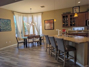 Una cocina moderna con una isla central, comedor con sillas y un amplio ventanal con cortinas.