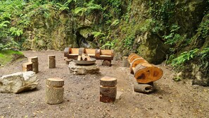 Eine Waldlichtung mit einem rustikalen Lagerfeuerplatz, Holzscheiten und einem großen, gefallenen Baumstamm.