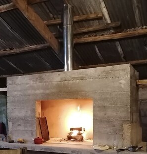 Ein rustikales Interieur mit Kamin aus Beton, einem Metallschornstein und einem schlichten Regal mit Topf und Glas.
