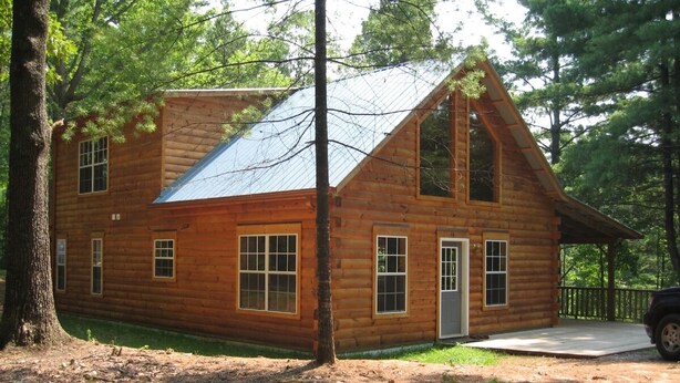 Une cabane en rondins avec un toit en pente, de nombreuses fenêtres et une véranda.