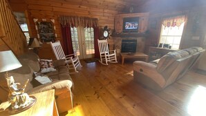 L’intérieur chaleureux d’un chalet avec un plancher en bois, une cheminée, un téléviseur et un fauteuil à bascule.