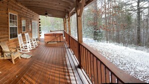 Une cabane en bois avec une véranda, des fauteuils à bascule et une vue sur une forêt enneigée.