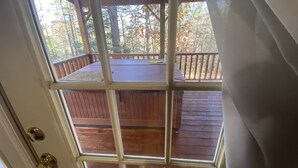 Une terrasse en bois avec une rambarde, une porte dotée d’un panneau de verre et une vue sur les arbres par la fenêtre.