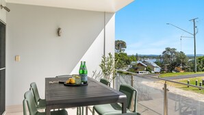 A balcony with a table set for two, featuring a bottle of Pellegrino water, lemons, and glasses. - Pilotage 3 - Lighthouse Views & Coastal Living in the Heart of Yamba - Holiday Yamba (YAMBA)