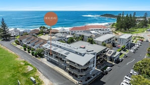 A coastal hotel with multiple buildings, a parking lot, and a view of the ocean. - Pilotage 3 - Lighthouse Views & Coastal Living in the Heart of Yamba - Holiday Yamba (YAMBA)