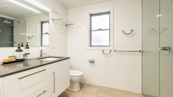 A modern bathroom with a glass shower enclosure, a white toilet, and a vanity with a mirror and sink. - Pilotage 3 - Lighthouse Views & Coastal Living in the Heart of Yamba - Holiday Yamba (YAMBA)