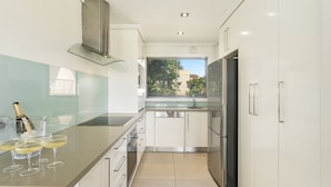 A modern kitchen with a glass island, stainless steel appliances, and a view of the outdoors. - Pilotage 3 - Lighthouse Views & Coastal Living in the Heart of Yamba - Holiday Yamba (YAMBA)