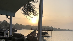 Ein überdachter Außenbereich mit Korbmöbeln und Blick auf ein Gewässer bei Sonnenuntergang.