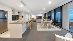 Une cuisine moderne avec un îlot central, un coin repas offrant une vue sur la mer et un salon doté d’une grande télévision.
