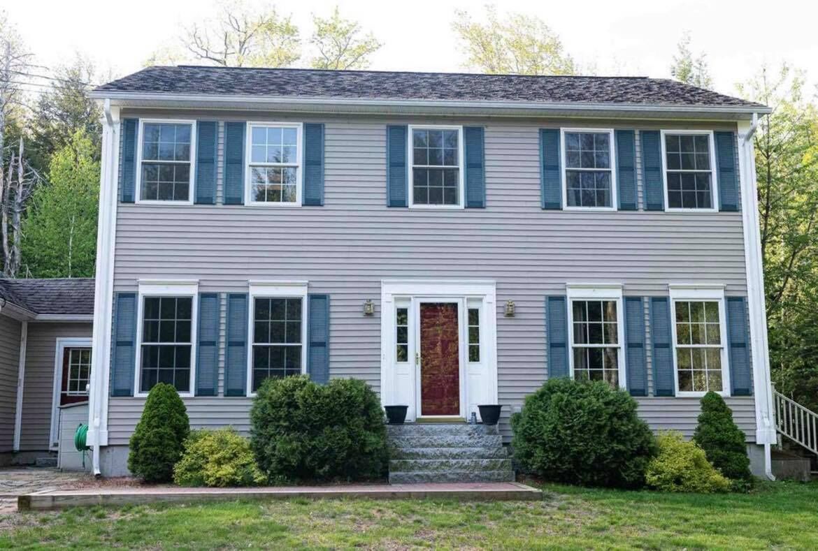 A two-story house with a front porch, a red door, and a small front yard with trimmed bushes.